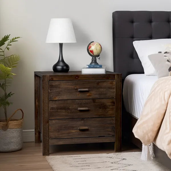 Wooden nightstand with lamp and decorative items next to a bed with a tufted headboard.