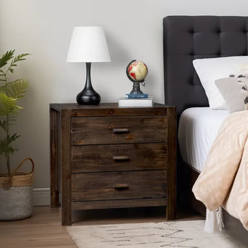 Wooden nightstand with lamp and decorative items next to a bed with a tufted headboard.